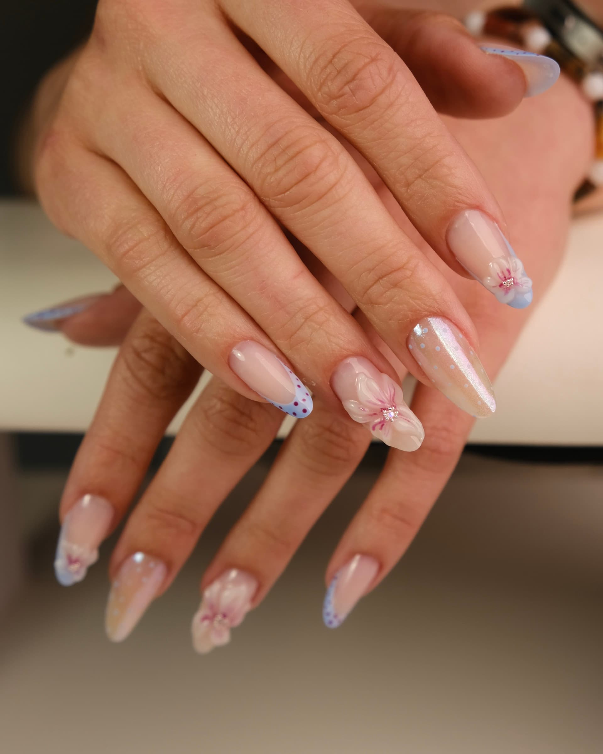 Long coffin-shaped nails with iridescent glitter, pale blue French tips, and 3D hand-painted flowers