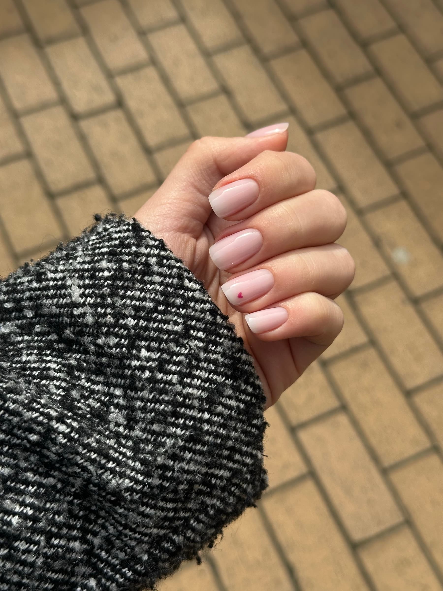 Short glossy nude nails with a single tiny pink heart accent