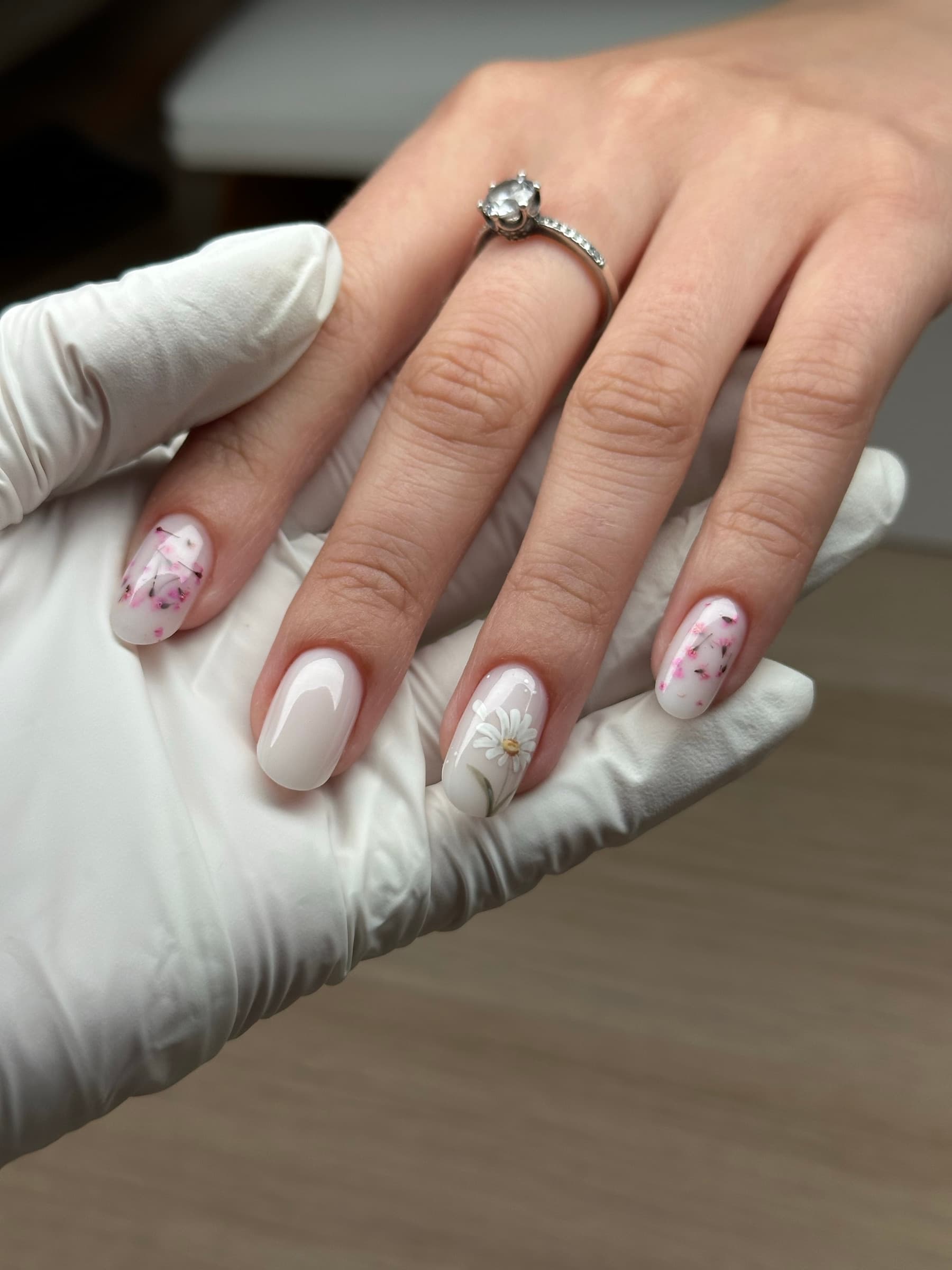 Short oval nails with delicate hand-painted cherry blossom sprigs on a milky white base