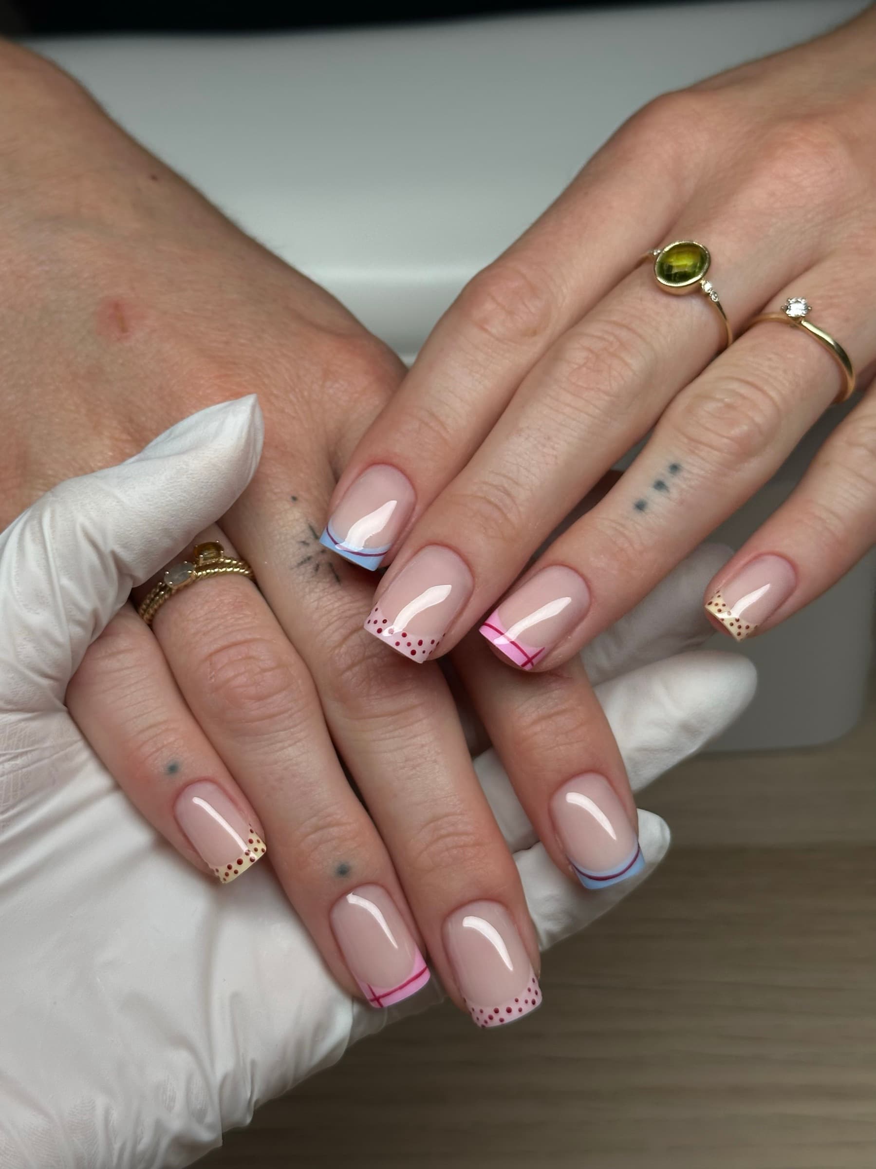 Nude nails with alternating pastel pink and blue French tips and fine dotted line accents