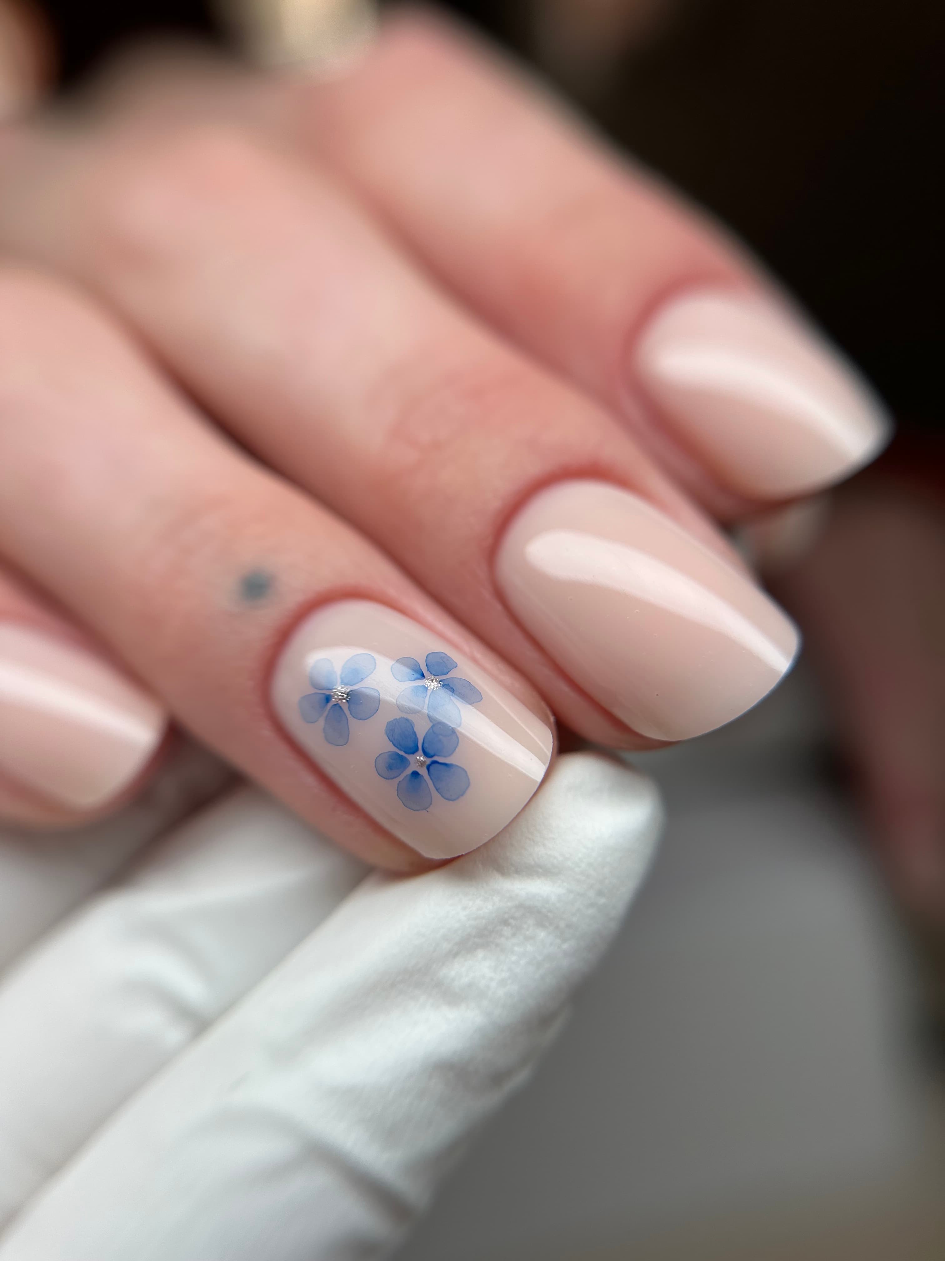 Short square milky nude nails with a single accent nail featuring hand-painted blue watercolor flowers